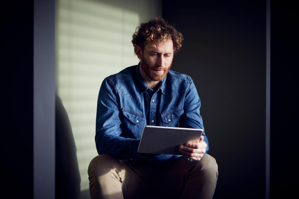 Casual businessman sitting down using a tablet to shop e-commerce