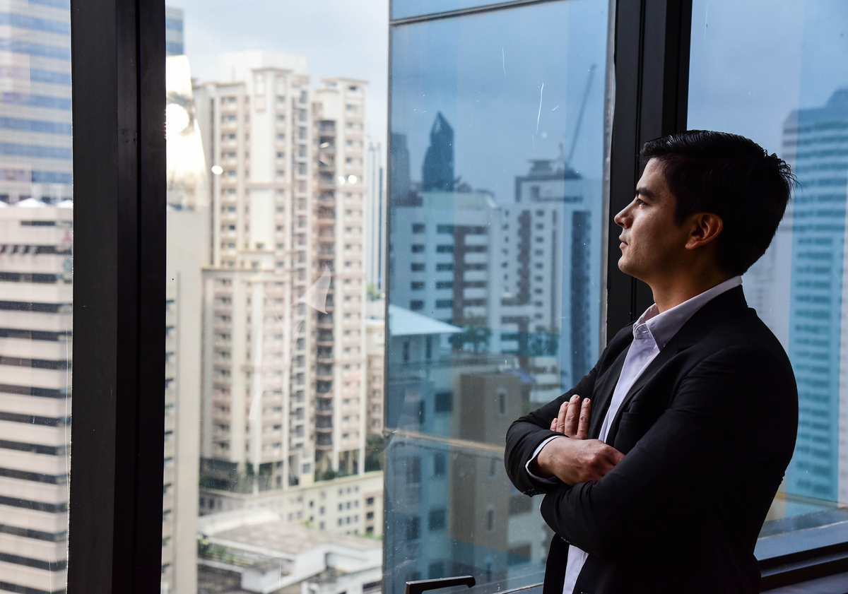 A handsome businessman look out of his office window on the tall building and think about the company development and new project in the future/Vision/Business going forwar
