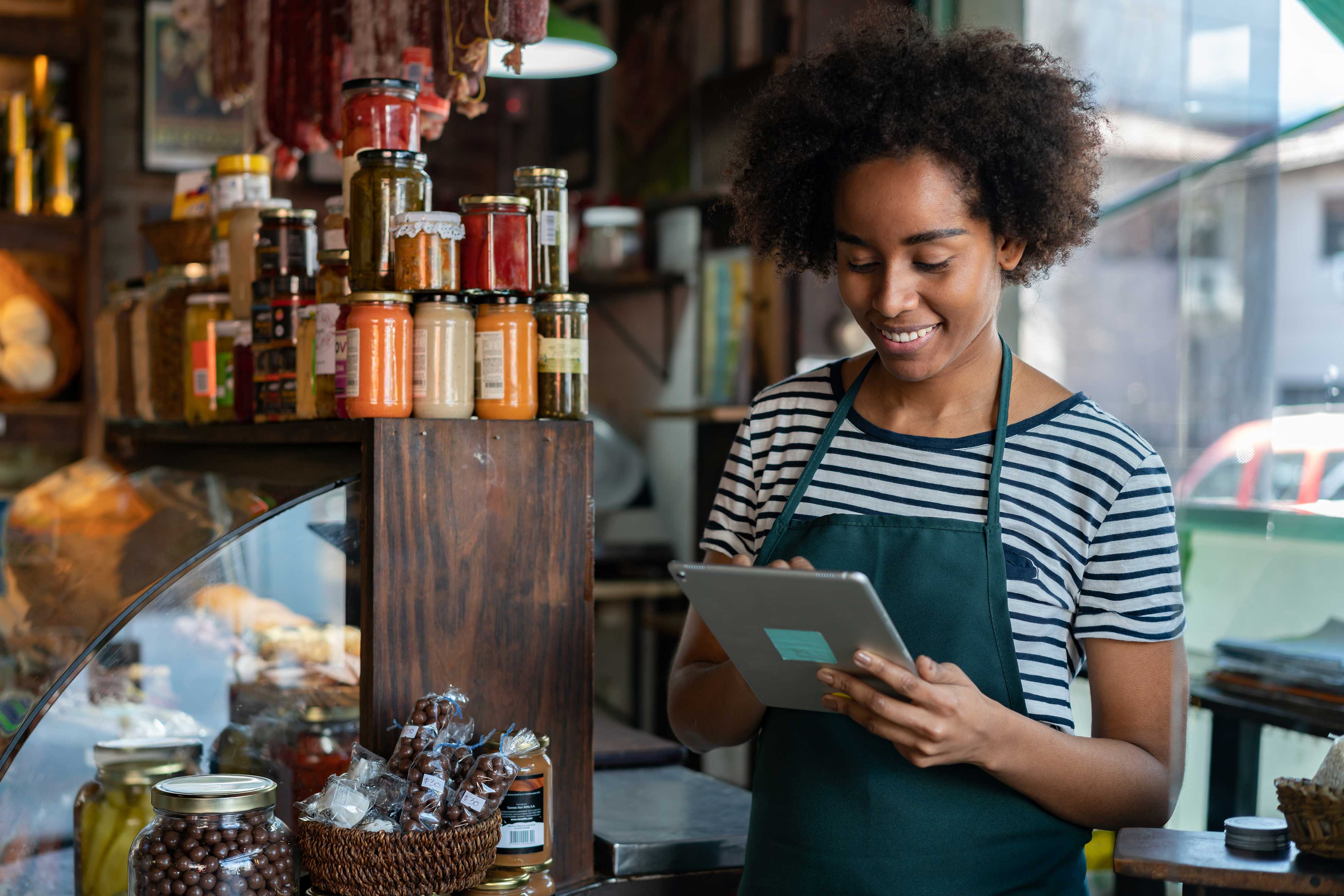 Multiracial female barista smiling while looking at a tablet