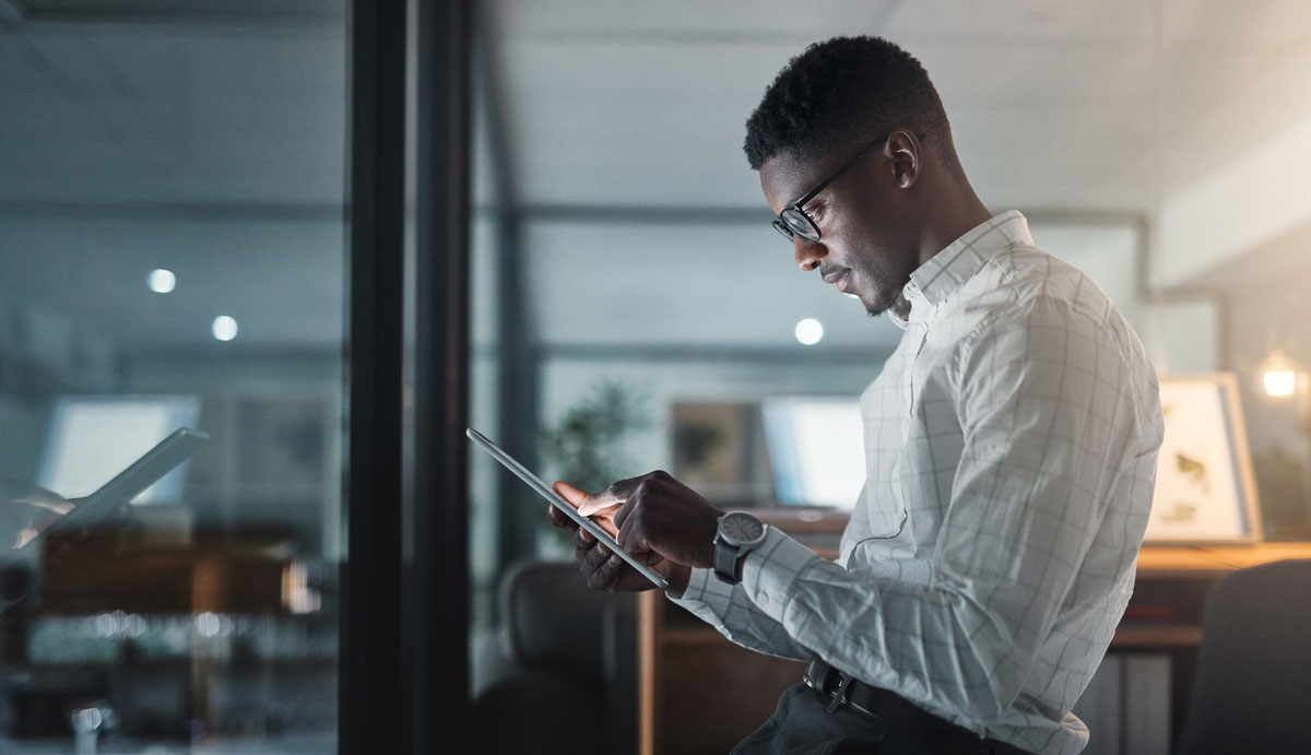 A man with glasses and a white shirt using a tablet in an office setting