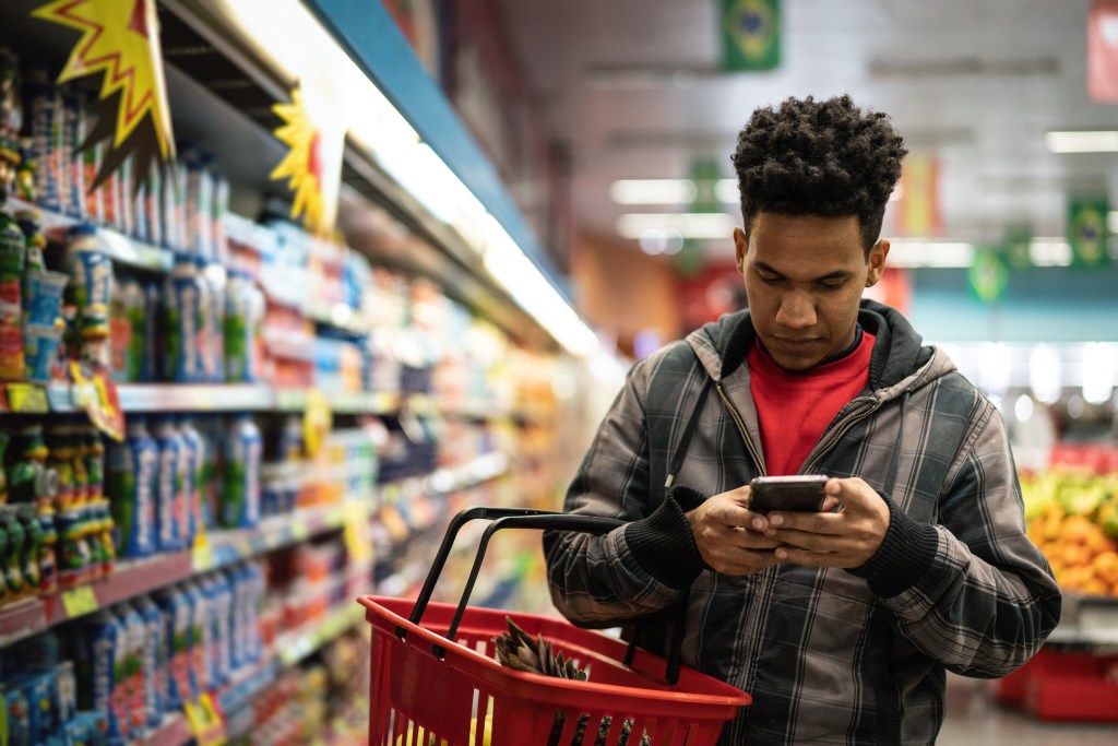 A man shopping at a grocery store checking his phone to review on pricing during times of inflation