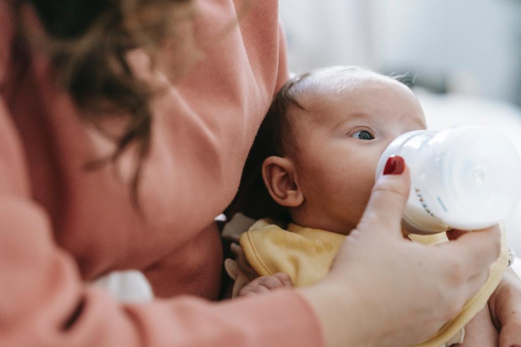 A woman feeding an infant with a bottle of baby formula