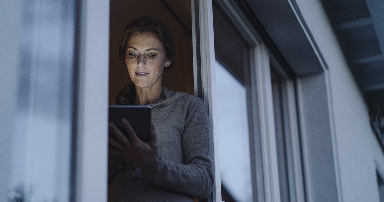 Woman standing in balcony door, using digital tablet