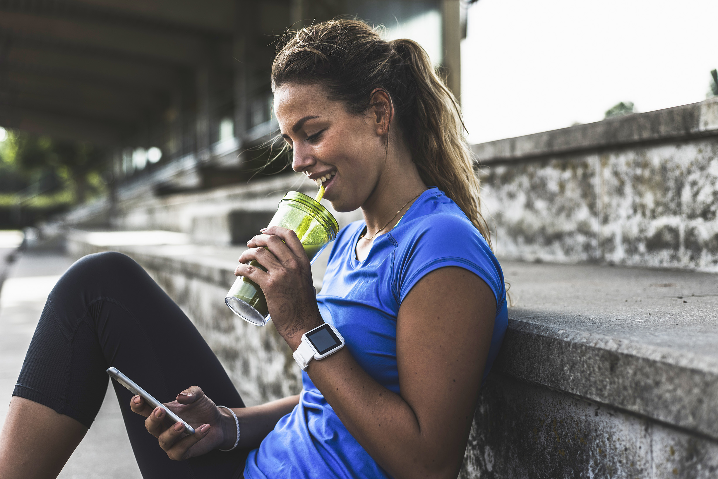 Young woman sitting on step with cell phone and drinking cup