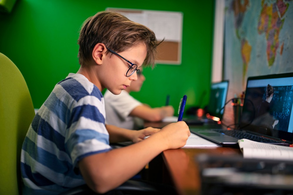 Two boys doing homework on laptops during school.