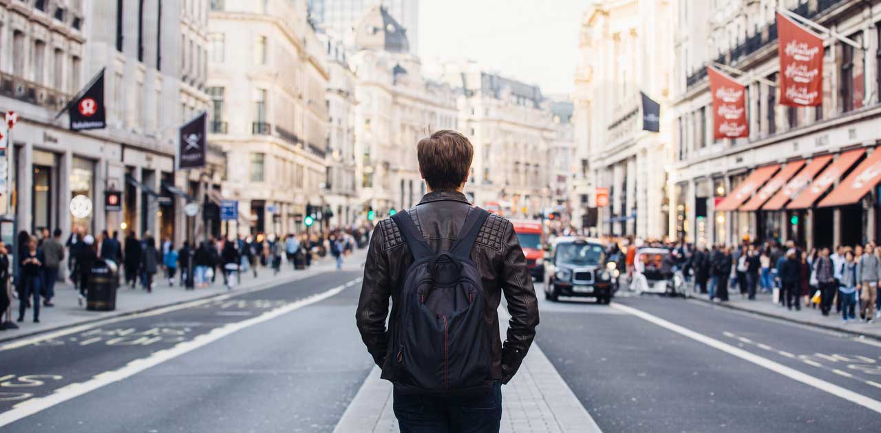 Man with leather coat and backpack looking down a busy street