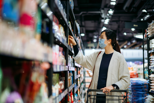 Young Asian woman shopping for groceries reading product label in supermarket