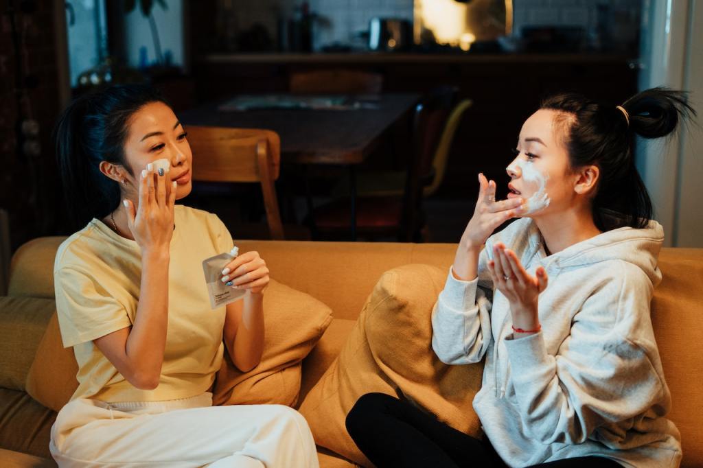 Two Asian American women sitting on a couch applying beauty products