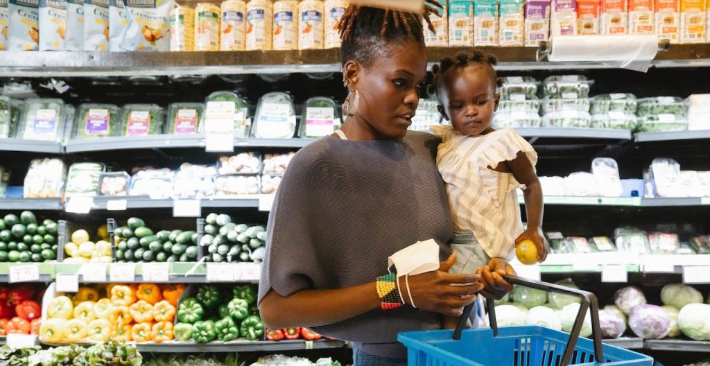 A woman at the grocery store holding a basket and baby