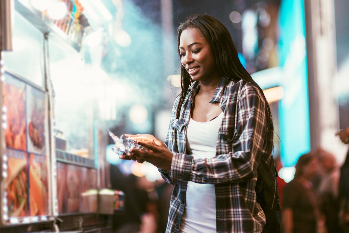 African American woman eats a hot dog at the end the end of her shopper journey