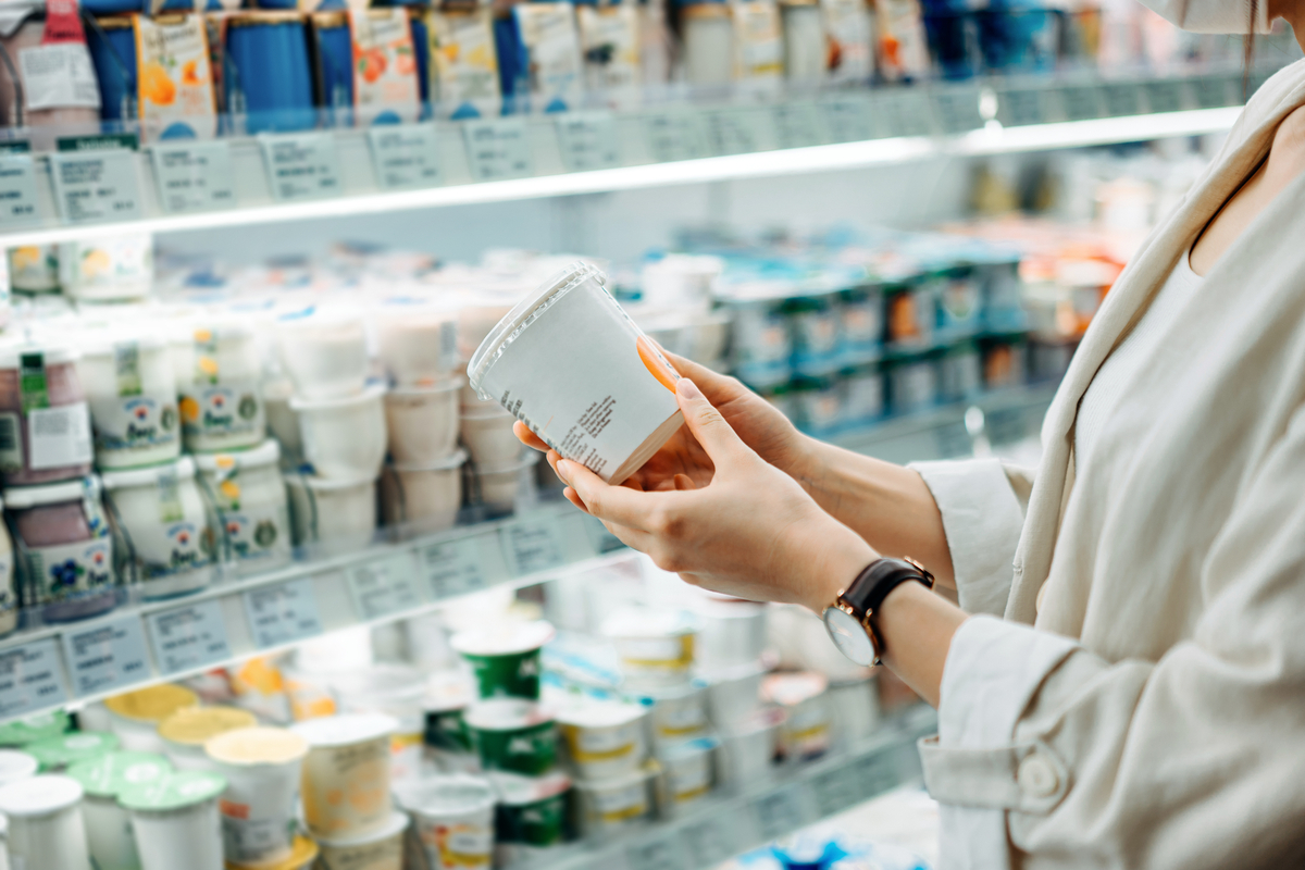 Cropped shot of young Asian woman shopping in the dairy section of a supermarket. She is reading the nutrition label on a container of fresh organic healthy natural yogurt