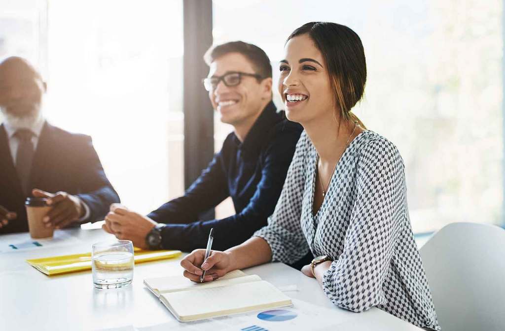 Business meeting with older man holding a coffee cup with a tie, a younger man with glasses and a blue shirt, and a young woman holding a pen and a notebook