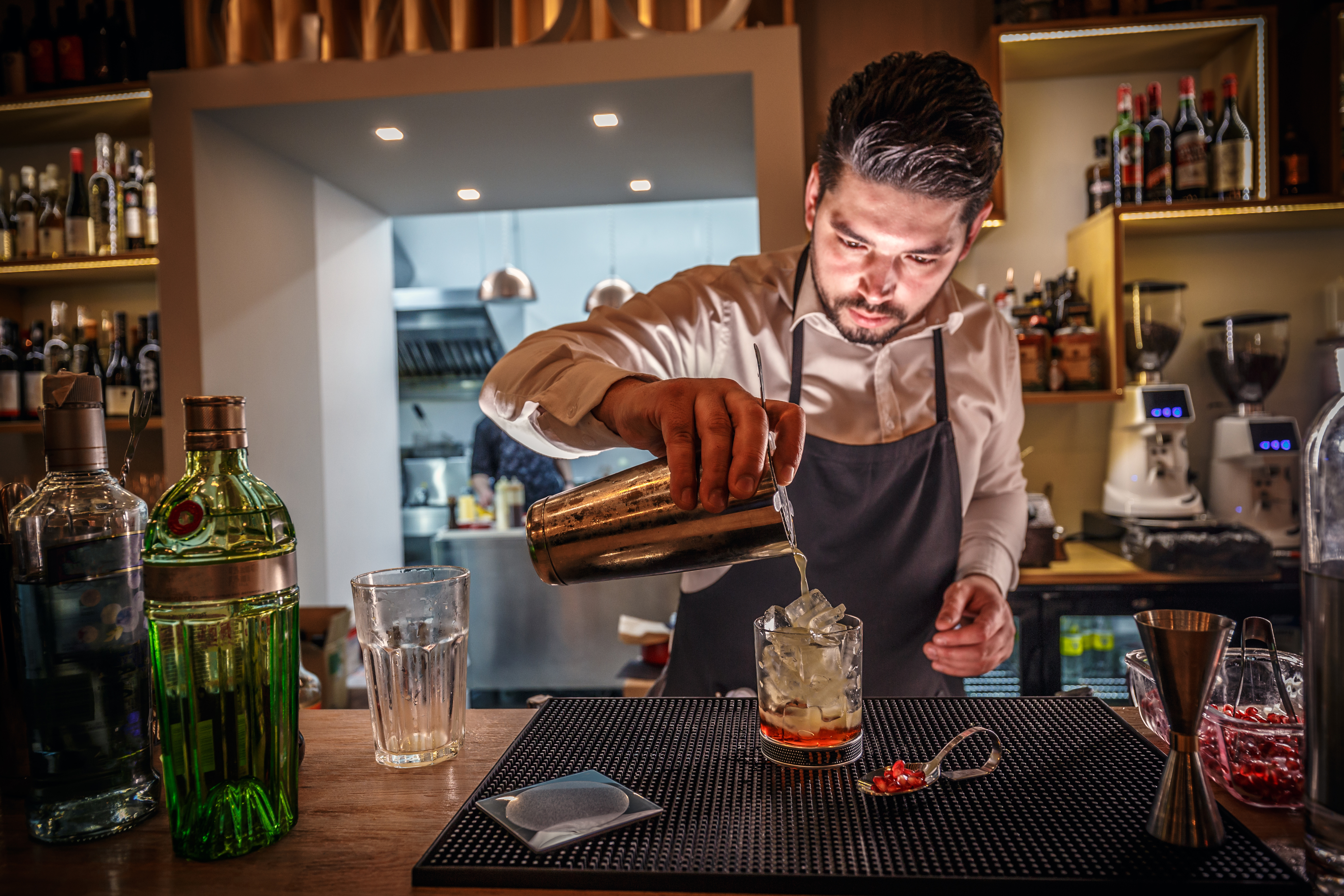 Male bartender is making cocktail pouring alcohol from shaker to glass at bar background