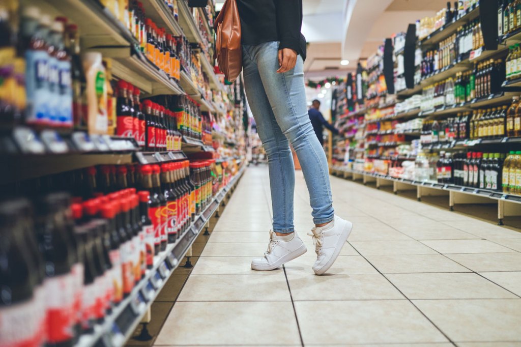 woman wearing jeans standing on her tiptoes to see more groceries
