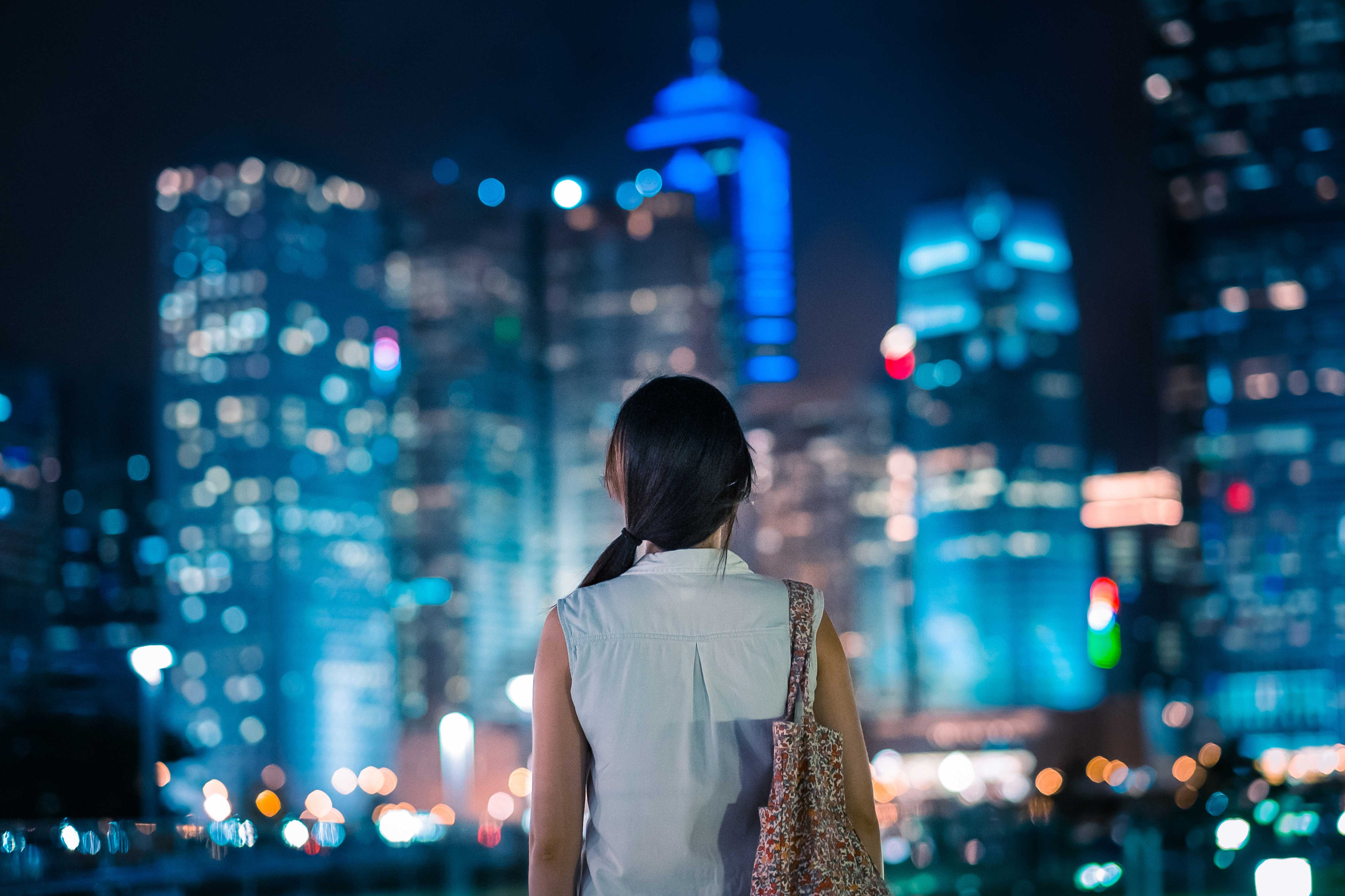 woman with dark hair facing away from the camera looking at a cityscape at night