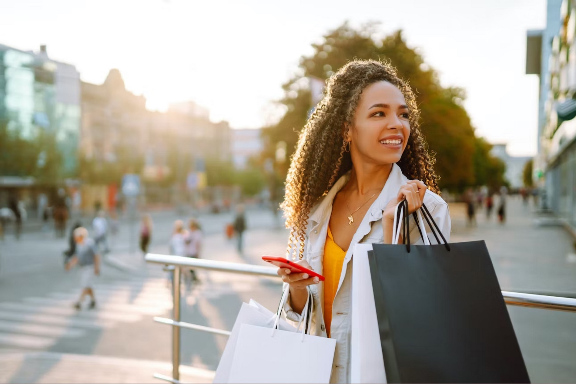 Woman with long curly hair holding multiple shopping bags and her mobile