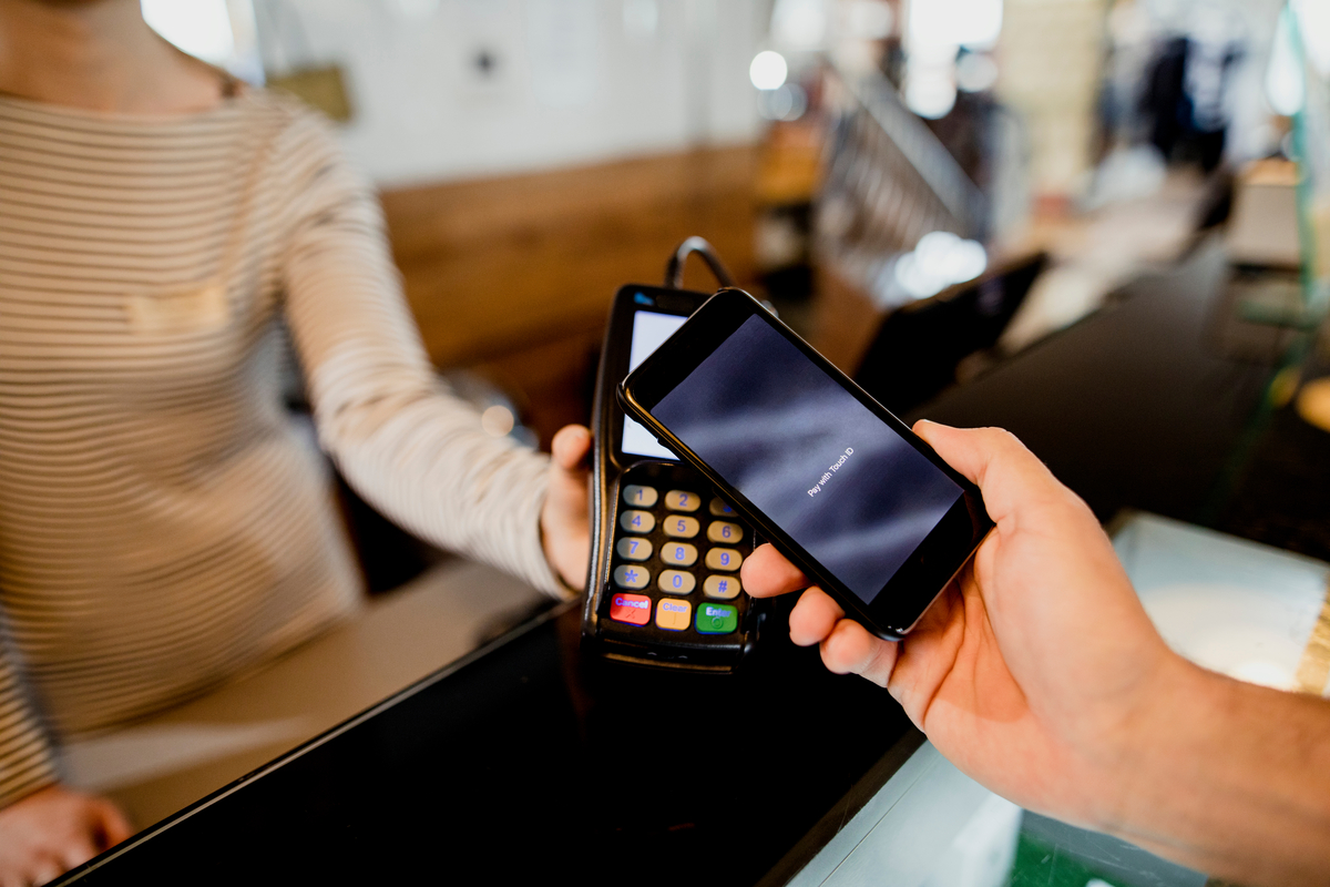 A young man in a fashionable clothing store, using his mobile phone to make a contactless payment