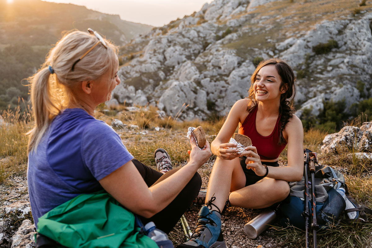 Mother And Daughter Eating Sandwiches On The Mountain After A Hike