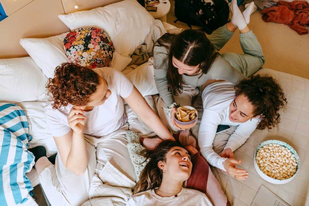 Group of teen girls laughing and eating on a bed at a sleepover
