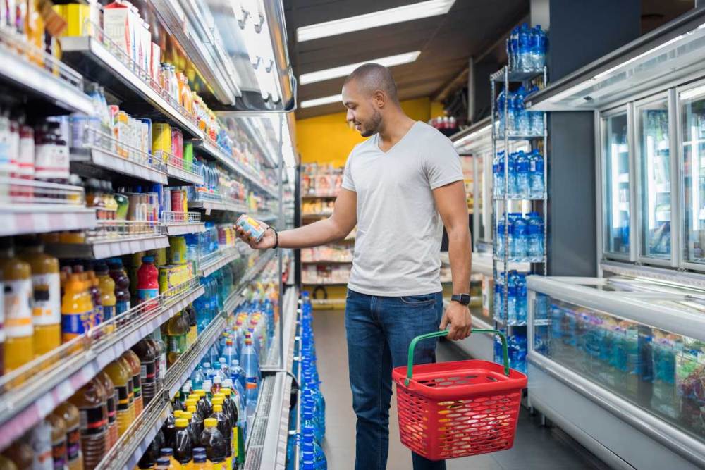 Man in jeans and a t-shirt holding a shopping basket looking at an items label in a store