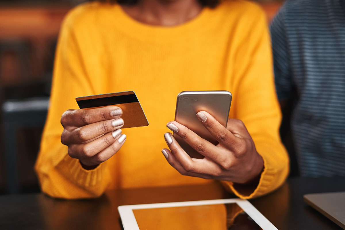 Woman with a golden shirt holding a credit card in one hand and a cellphone in the other.