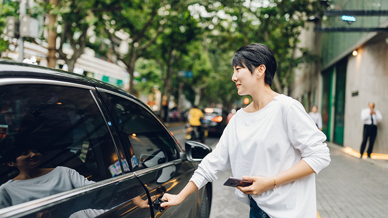 Asian woman with white shirt holding mobile phone entering a black car 