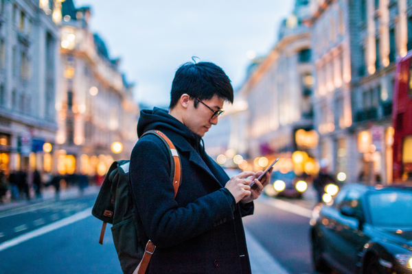 Asian man with backpack on street looking at phone