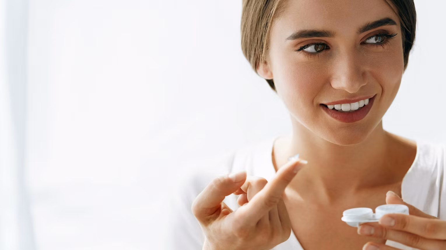 Beautiful young woman holding a contact lens on her fingertip