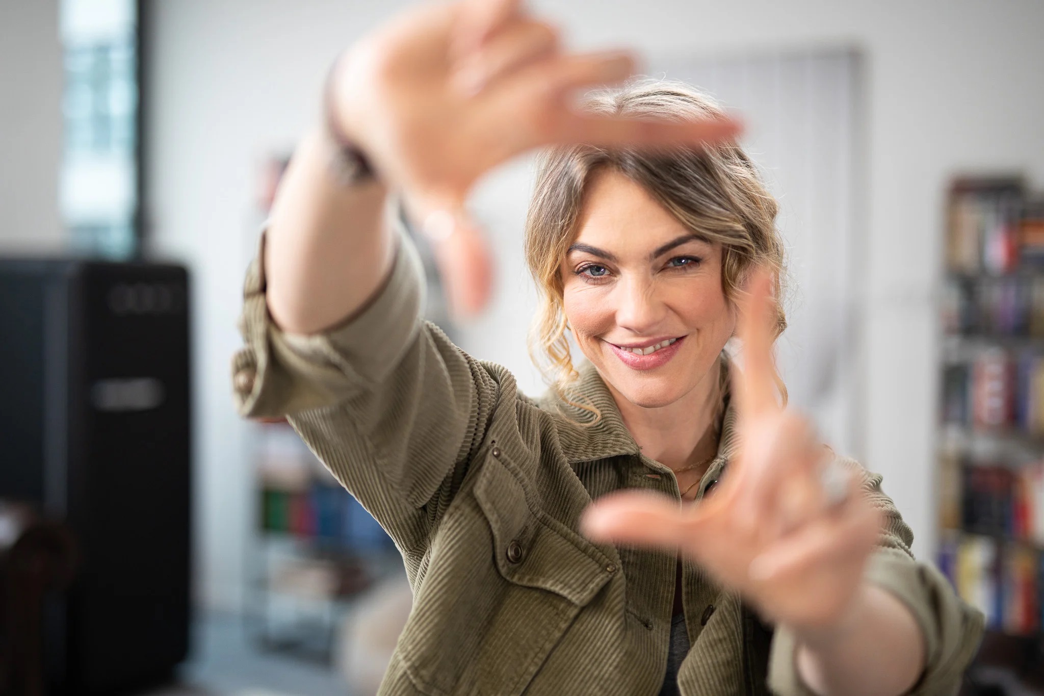 Woman in brown jacket holding her hands out framing her face