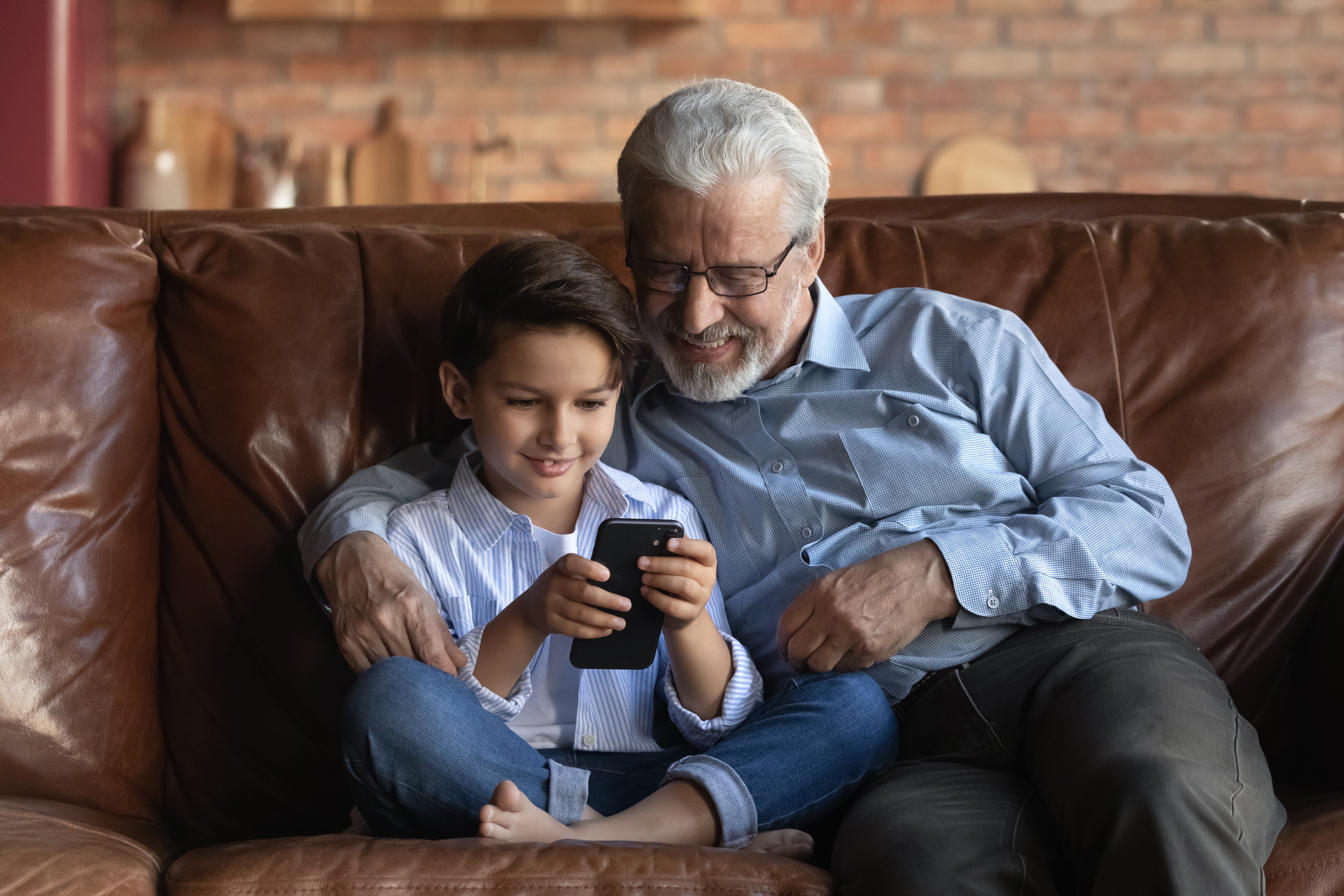 Boomer generation grandfather and grandson at home on the couch looking at a mobile device together