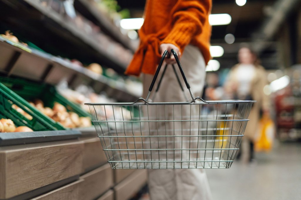 Woman in a thick orange sweater holding a metal wire shopping basket that is empty