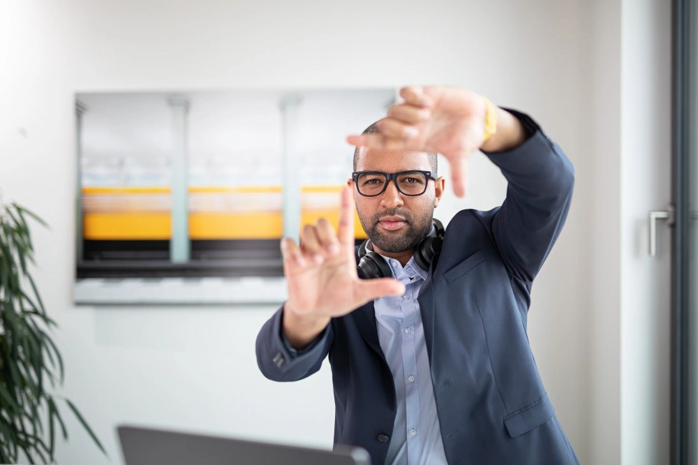 Man in blazer and blue shirt with thick glasses framing his face with his hands