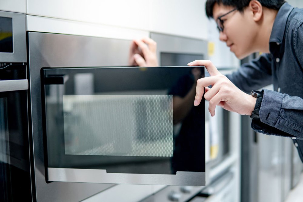 Asian man looking in a microwave