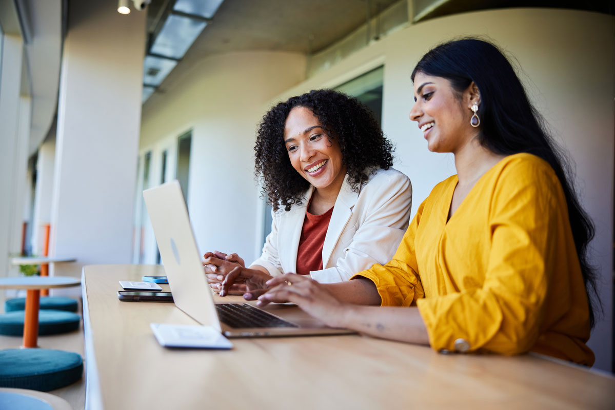 Two women working together on a laptop in a conference room.