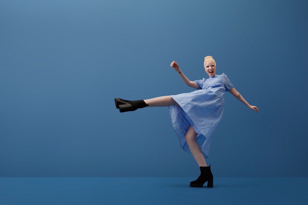 Full length portrait of albino young woman shouting while kicking leg against blue background