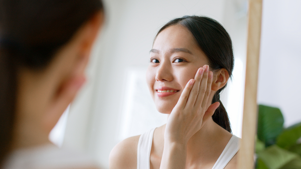Young Asian woman touching healthy facial skin look at mirror