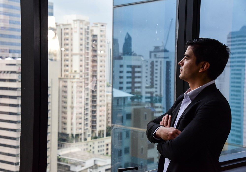 A handsome businessman look out of his office window on the tall building and think about the company development and new project in the future/Vision/Business going forwar