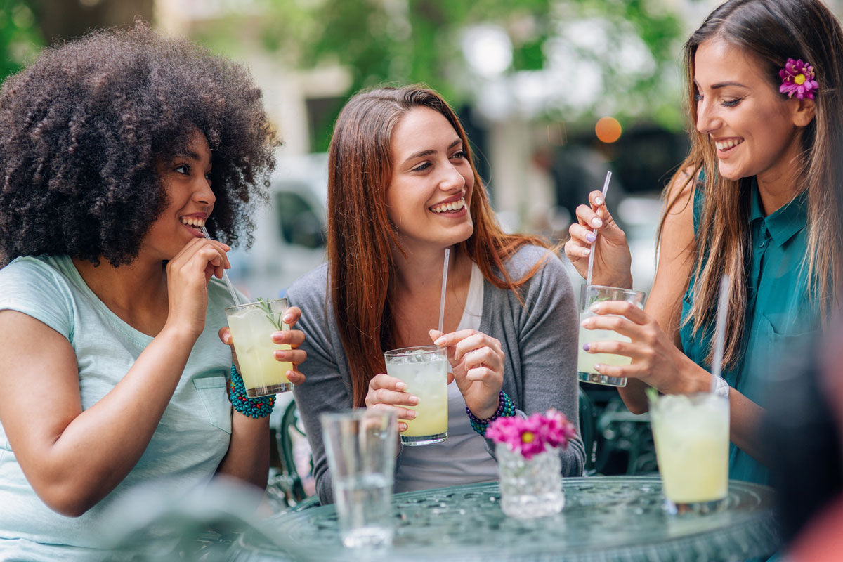 Three beautiful friends having iced drinks and gossips outdoor at summer day
