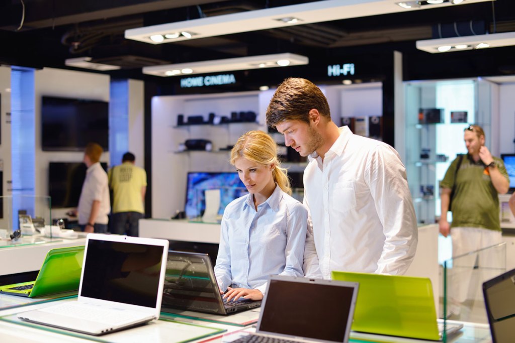 Young couple in consumer electronics store looking at latest laptop, television and photo camera