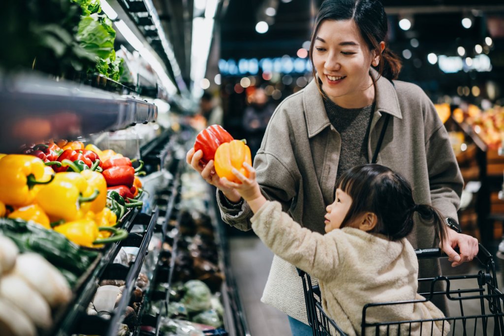 Asian mother and daughter shopping for fresh fruits and vegetables together joyfully in supermarket. They are picking up some fresh bell peppers along the produce aisle. Healthy eating lifestyle and habits. Making a healthier food choice for family