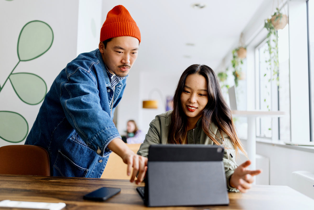 Two Asian co-workers working together on a tablet in an office setting