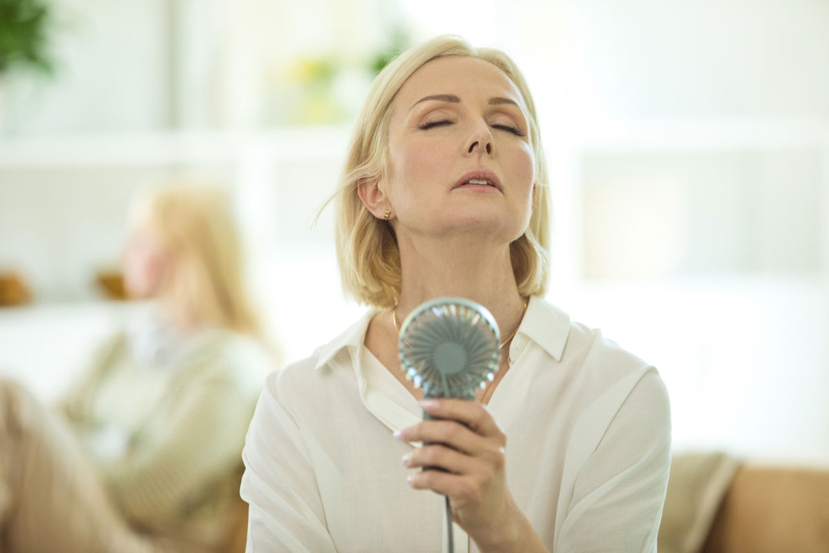 A middle-aged woman fans herself with a portable fan