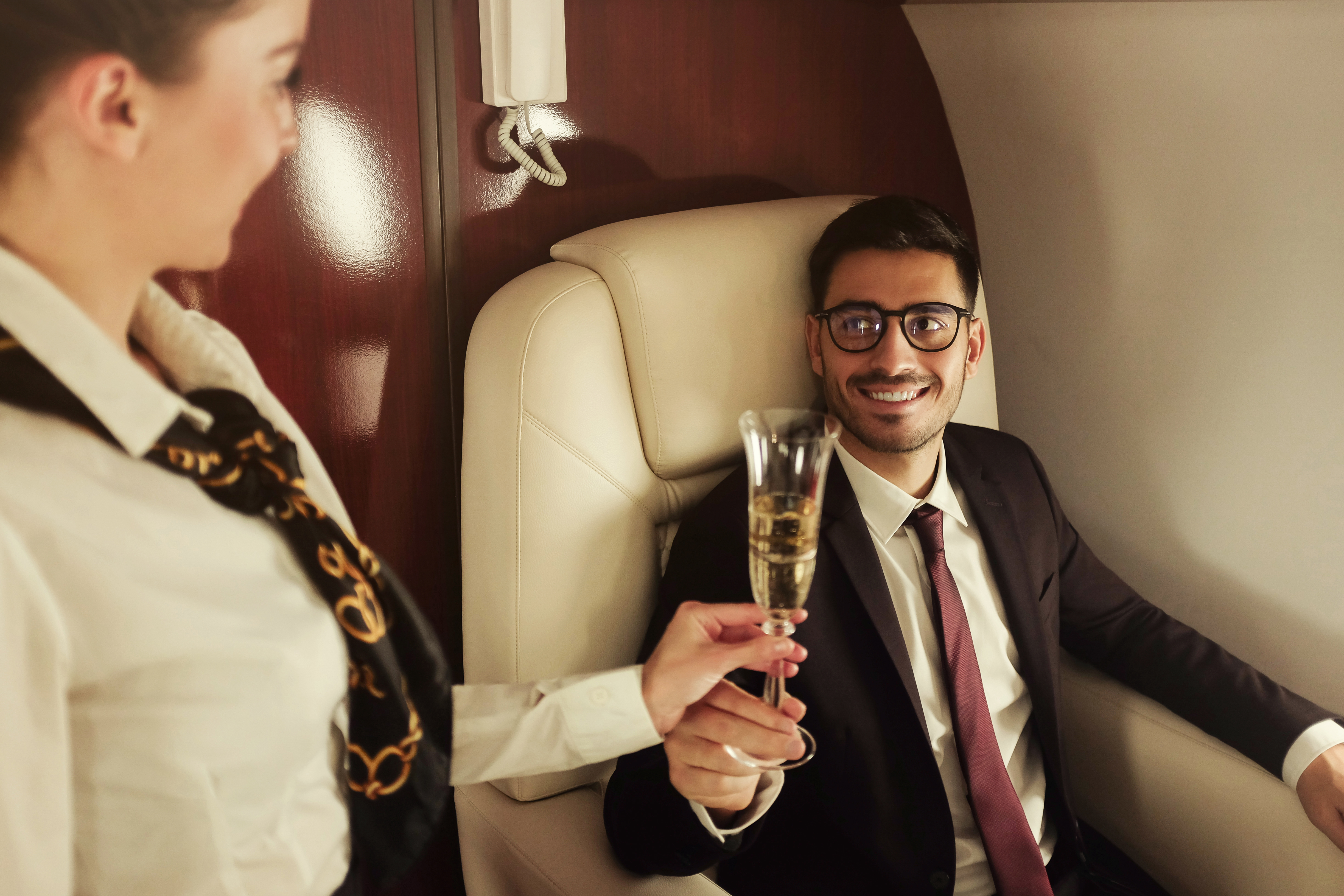 A flight attendant hands a businessman a glass of Champagne while traveling first-class