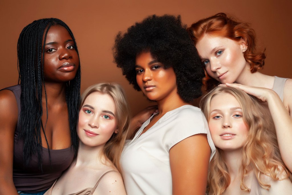 young pretty caucasian, afro, scandinavian woman posing cheerful together on brown background, lifestyle diverse nationality people concept