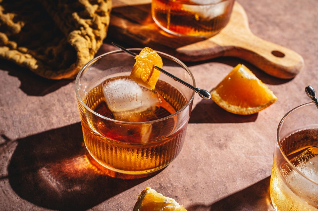 Cognac on the rocks with a twist of orange peel sat on a wooden counter