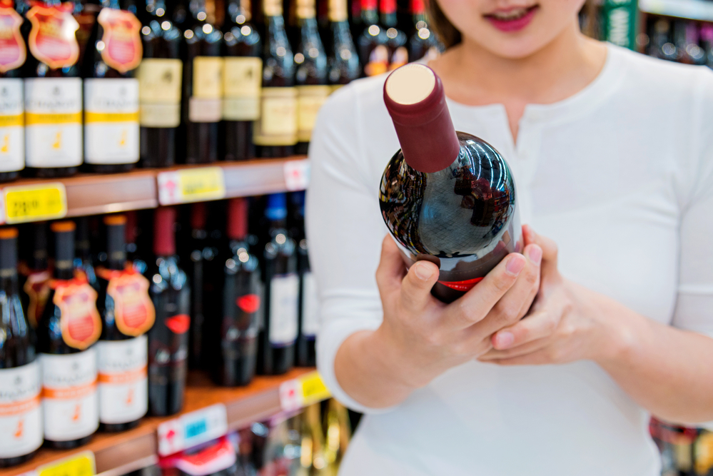 girl looking at a wine bottle in a supermarket
